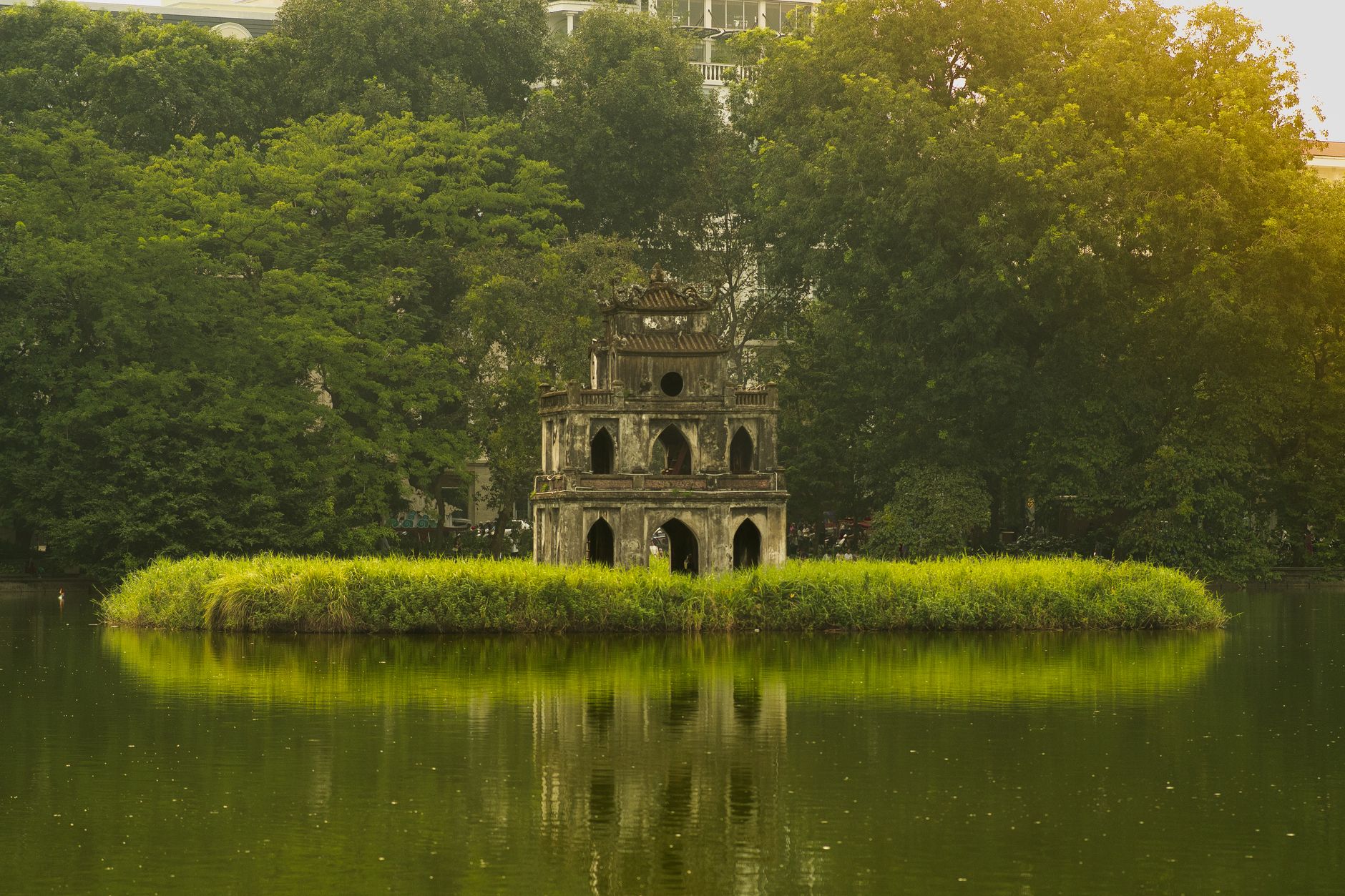 Serene view of Turtle Tower in Hanoi's Hoan Kiem Lake surrounded by lush greenery.