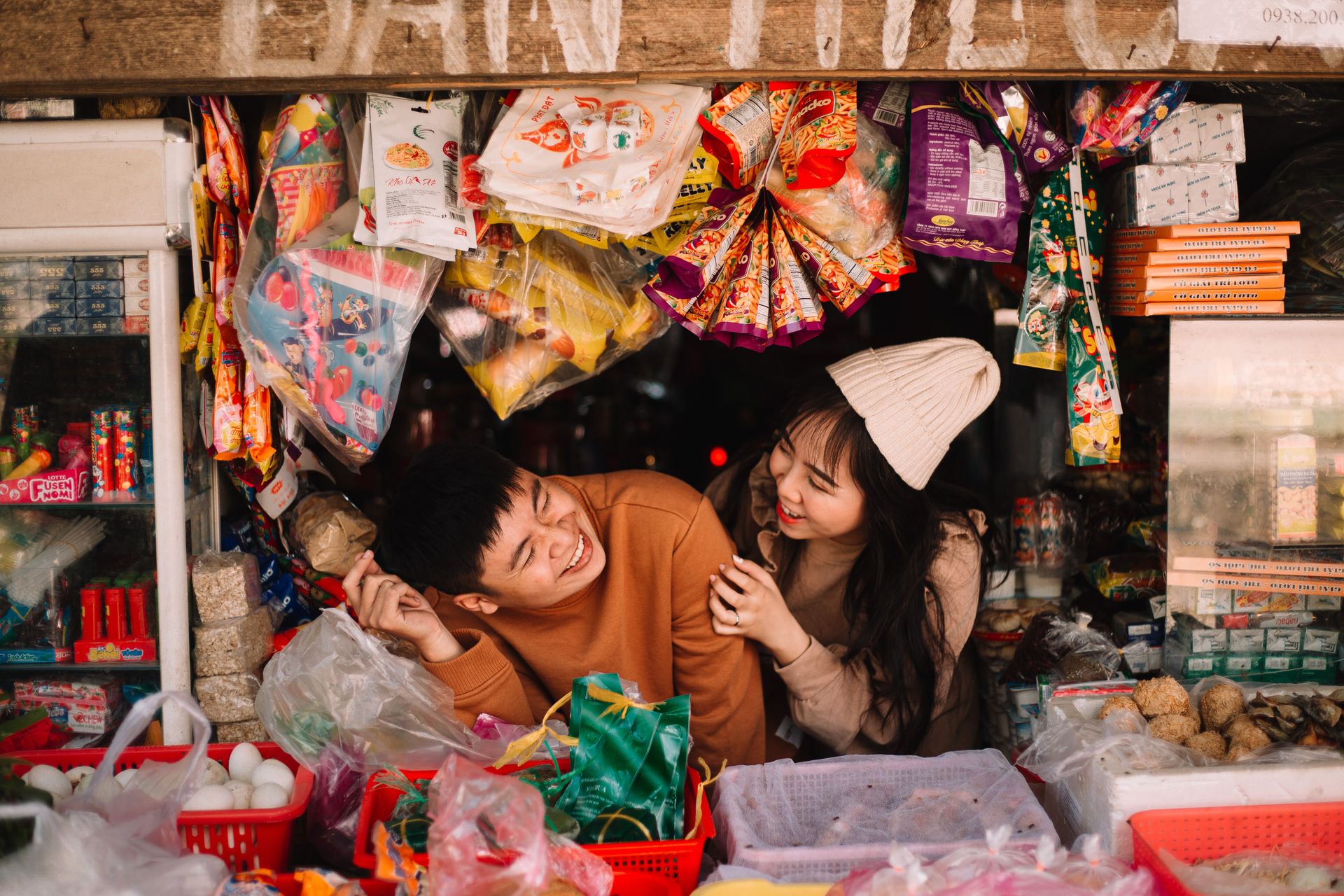 Happy couple enjoying time at a colorful, bustling market stall filled with various goods.
