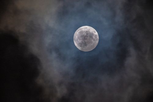 Free Atmospheric capture of a full moon glowing through dark clouds at night. Stock Photo