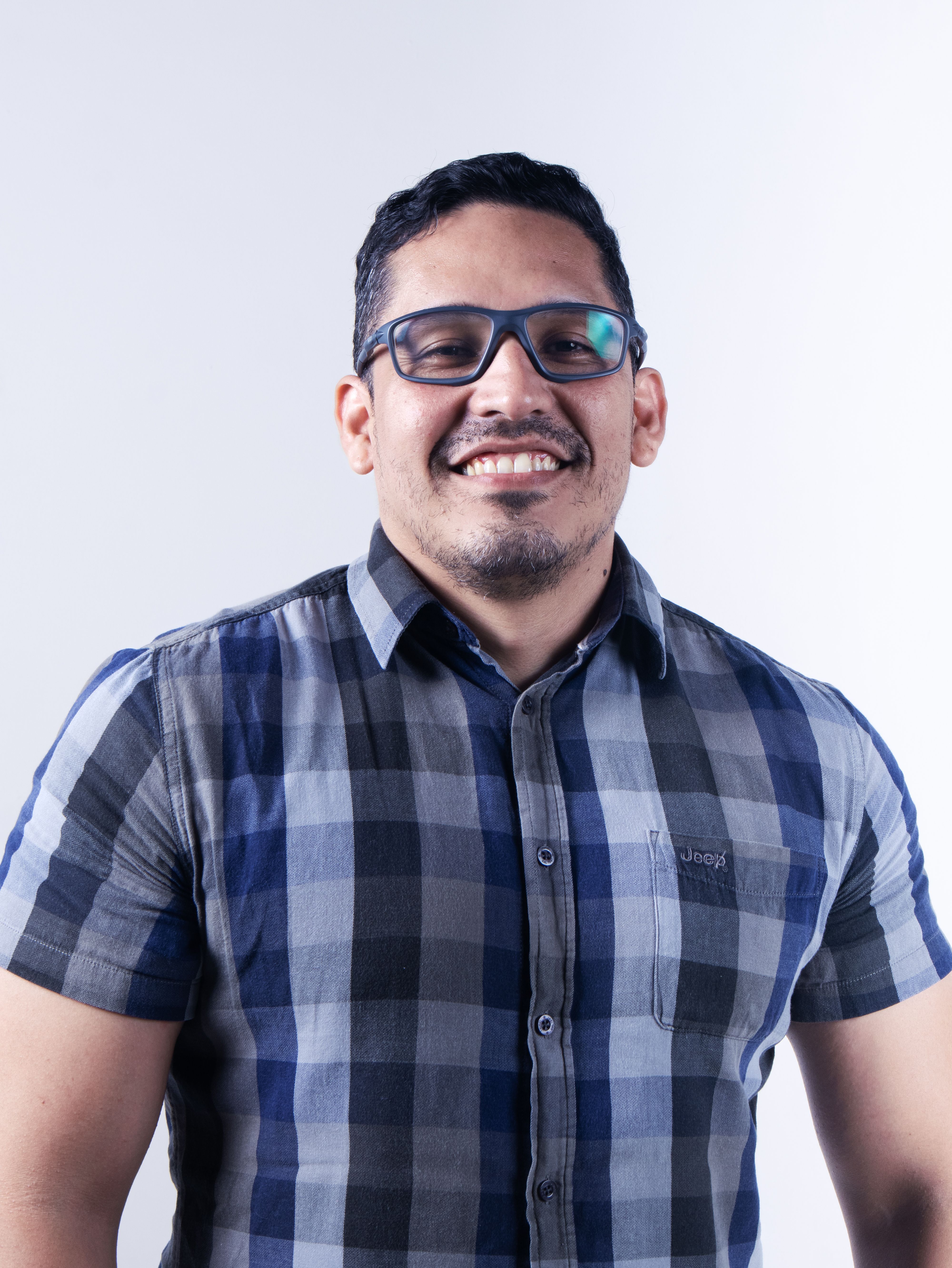 Portrait of a smiling man wearing a blue checkered shirt and glasses.