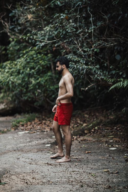 Free A lone man stands in red shorts on a forest path, surrounded by dense greenery. Stock Photo
