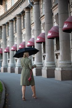 Woman walking on city sidewalk with an umbrella during a rainy day.