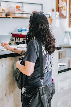 Young woman with curly hair orders at a coffee shop counter, exuding casual coffee shop vibes.