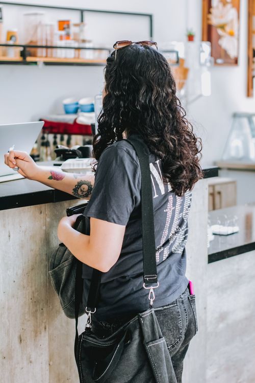 Free Young woman with curly hair orders at a coffee shop counter, exuding casual coffee shop vibes. Stock Photo