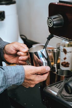 Close-up of hands steaming milk with an espresso machine in a cozy café environment.