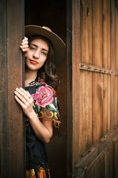 Beautiful young woman in traditional Mexican attire peeking from wooden door.