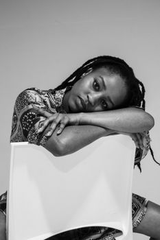 Black and white portrait of a woman resting on a chair, showcasing alternative fashion and introspection.