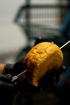 Gloved hands slicing a round loaf of bread with a sharp knife, dark background.