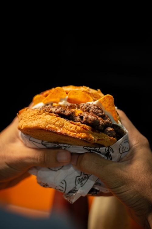 Free Tasty beef burger with toppings and crispy chips held by hands against dark background. Stock Photo