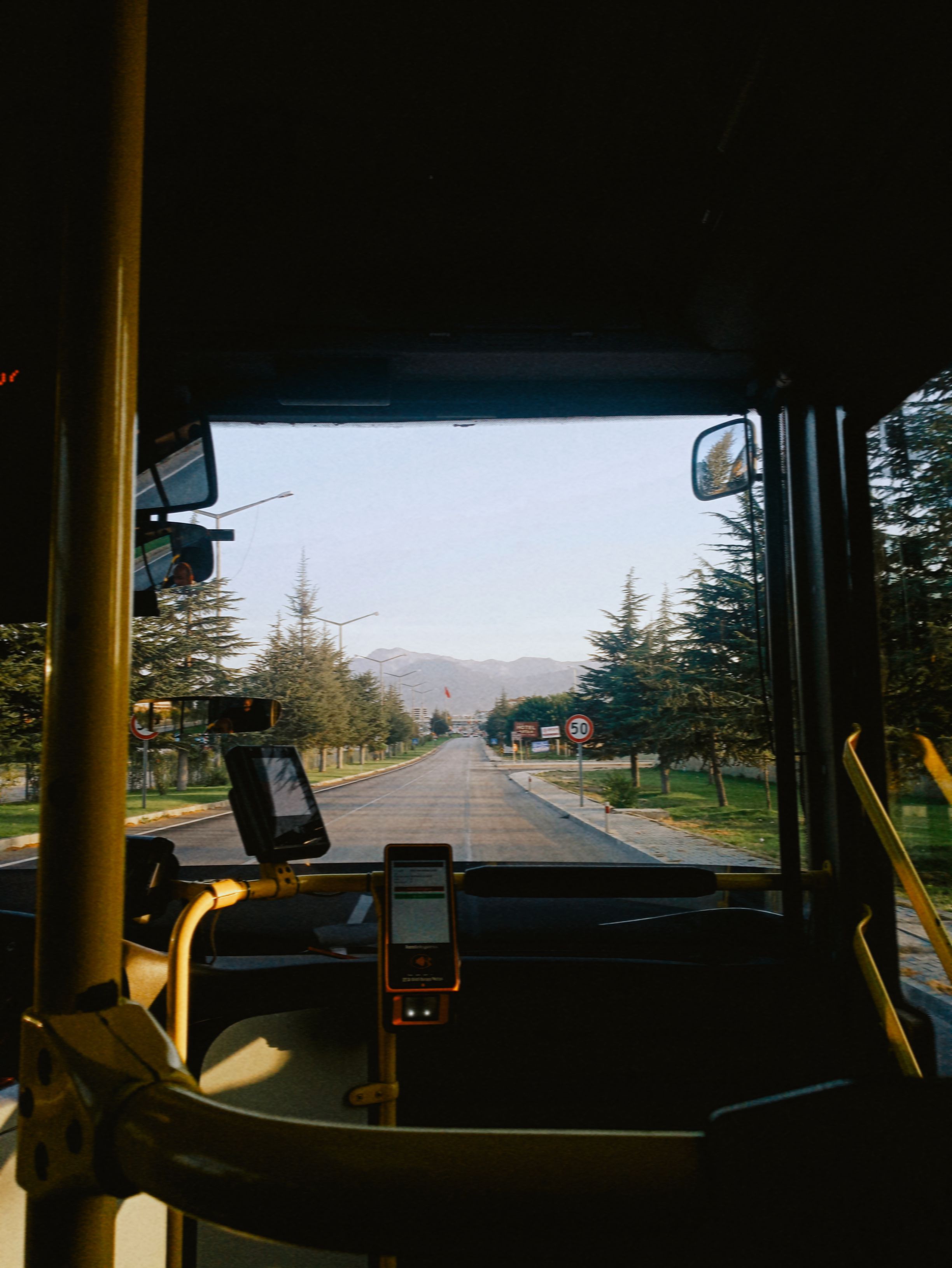 View from a bus front window showing a scenic road with trees and mountains