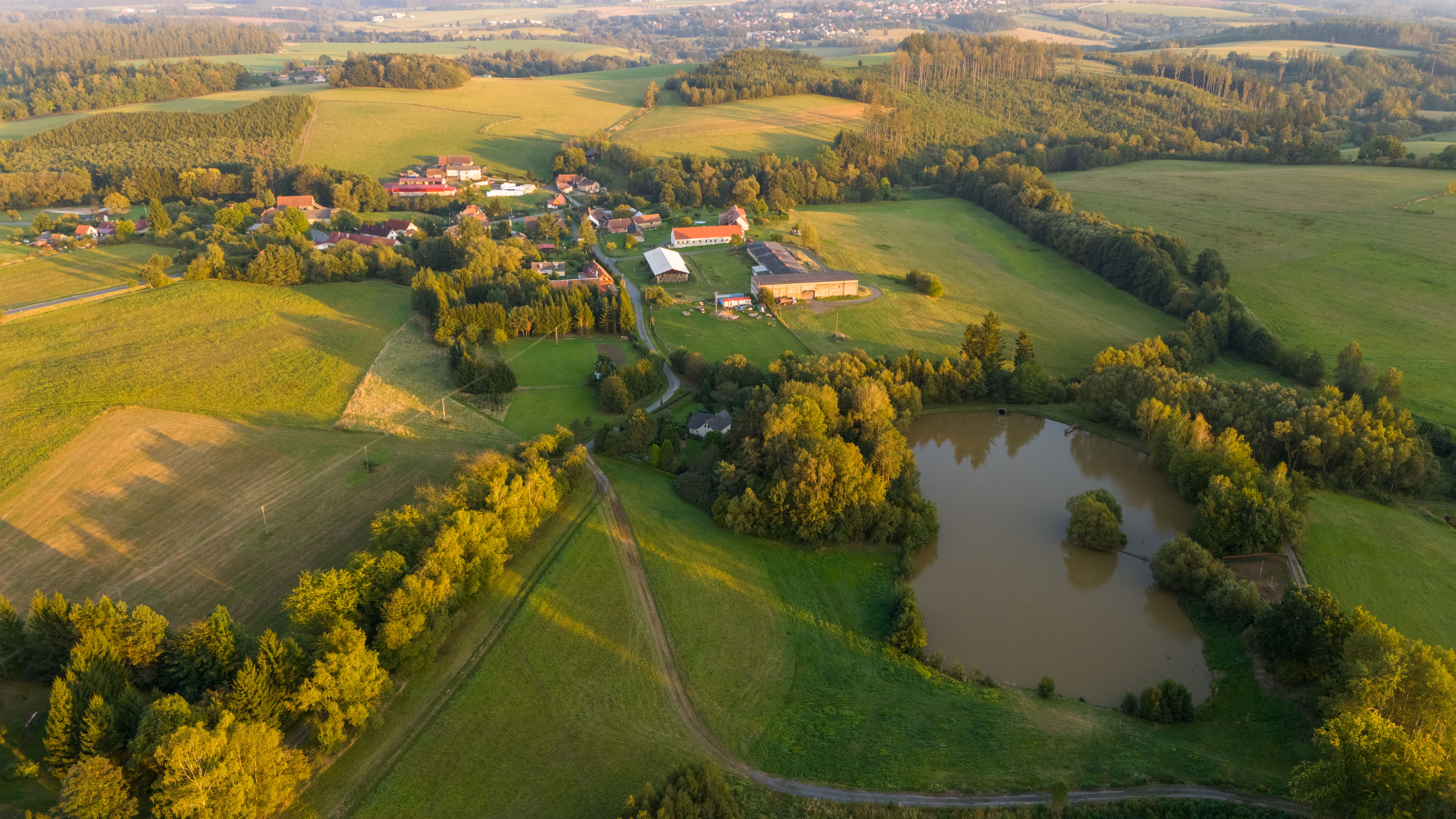 Stunning aerial view of Zbraslavice countryside with fields, forest, and pond at sunset.