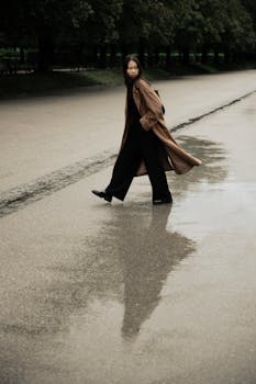 Stylish woman walking on a rainy street in Munich, reflecting in a puddle.