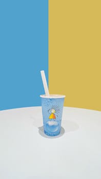 Artistic blue cup with a straw against a yellow and blue split background. Minimalist style.