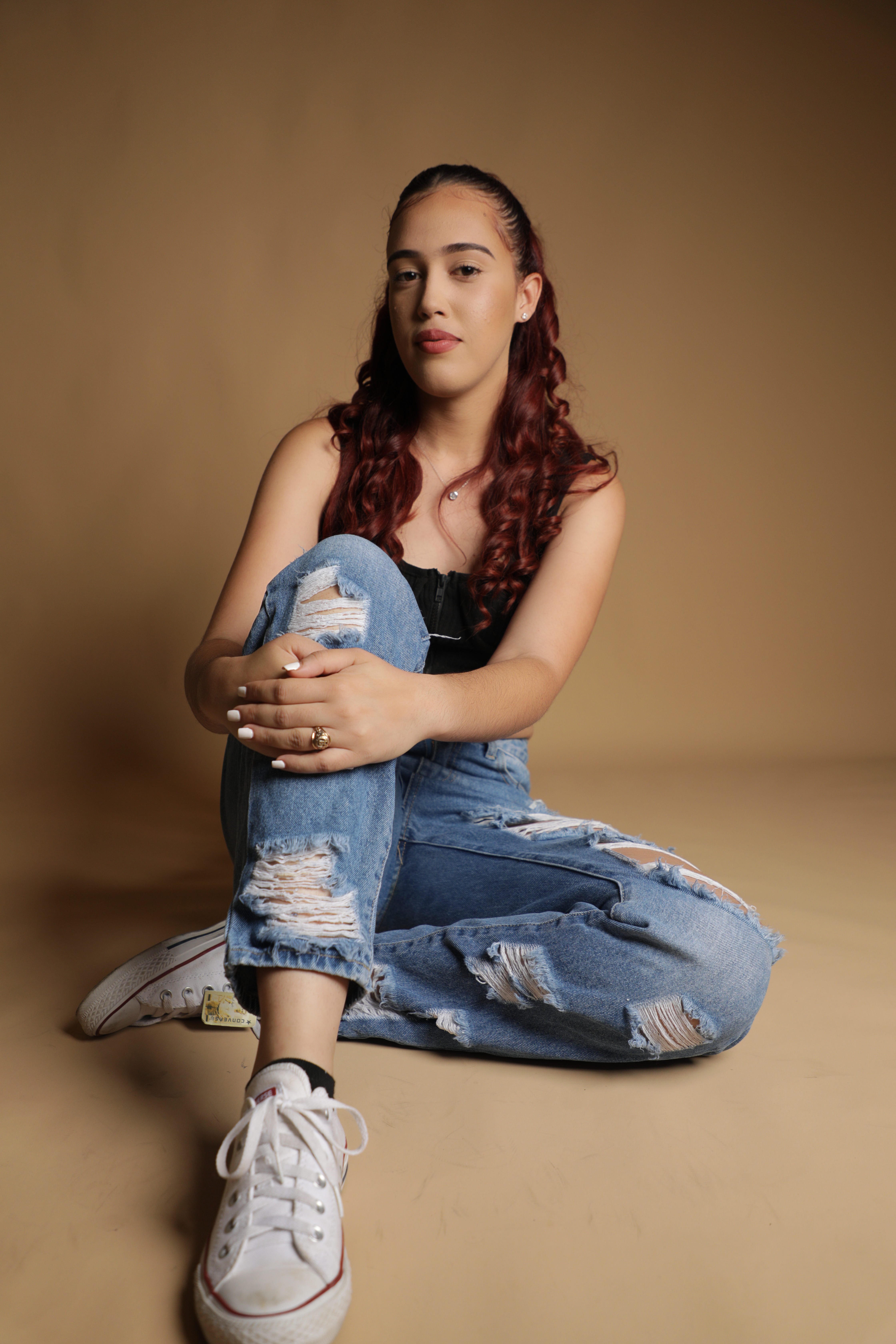 Portrait of a young woman in casual attire sitting in a studio setting.
