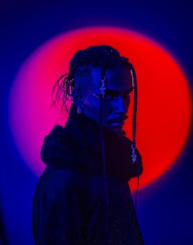 Dramatic portrait of a person with braided hair under neon red and blue lighting.