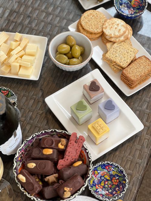 Free Variety of gourmet snacks including cheese, crackers, chocolates, and olives on a textured table. Stock Photo