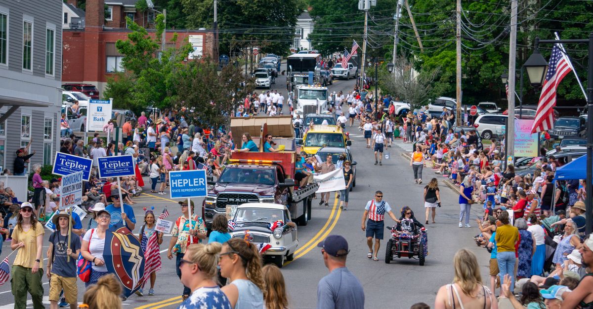 Crowds gather on a sunny day for a festive parade with colorful floats and banners.