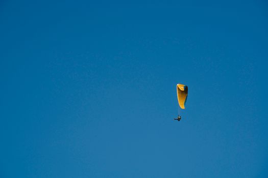 A solitary yellow paraglider glides against a vast, cloudless blue sky.