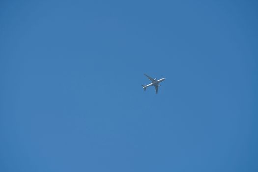 A commercial airplane soaring high against a clear blue sky, viewed from below.