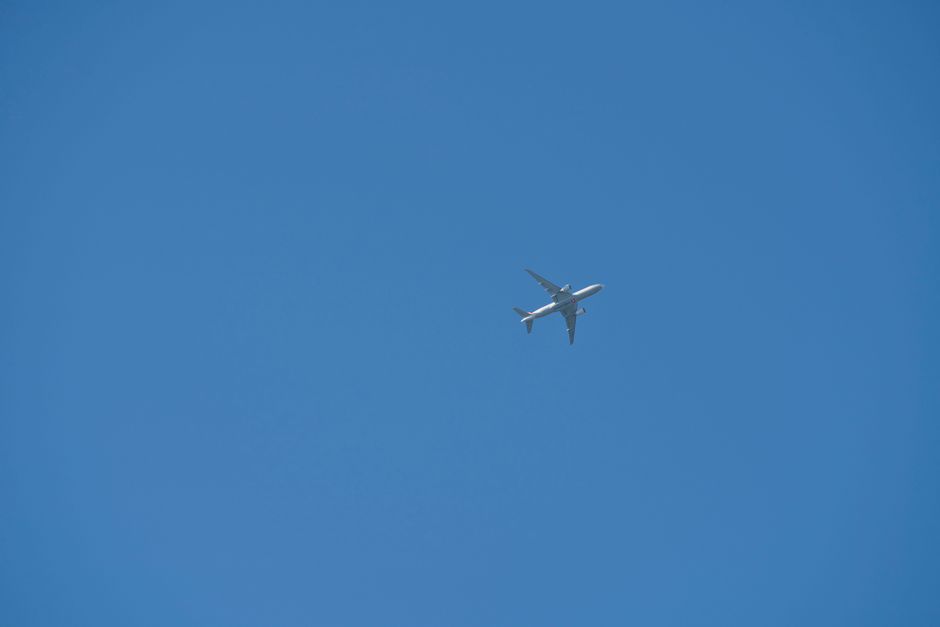 A commercial airplane soaring high against a clear blue sky, viewed from below.