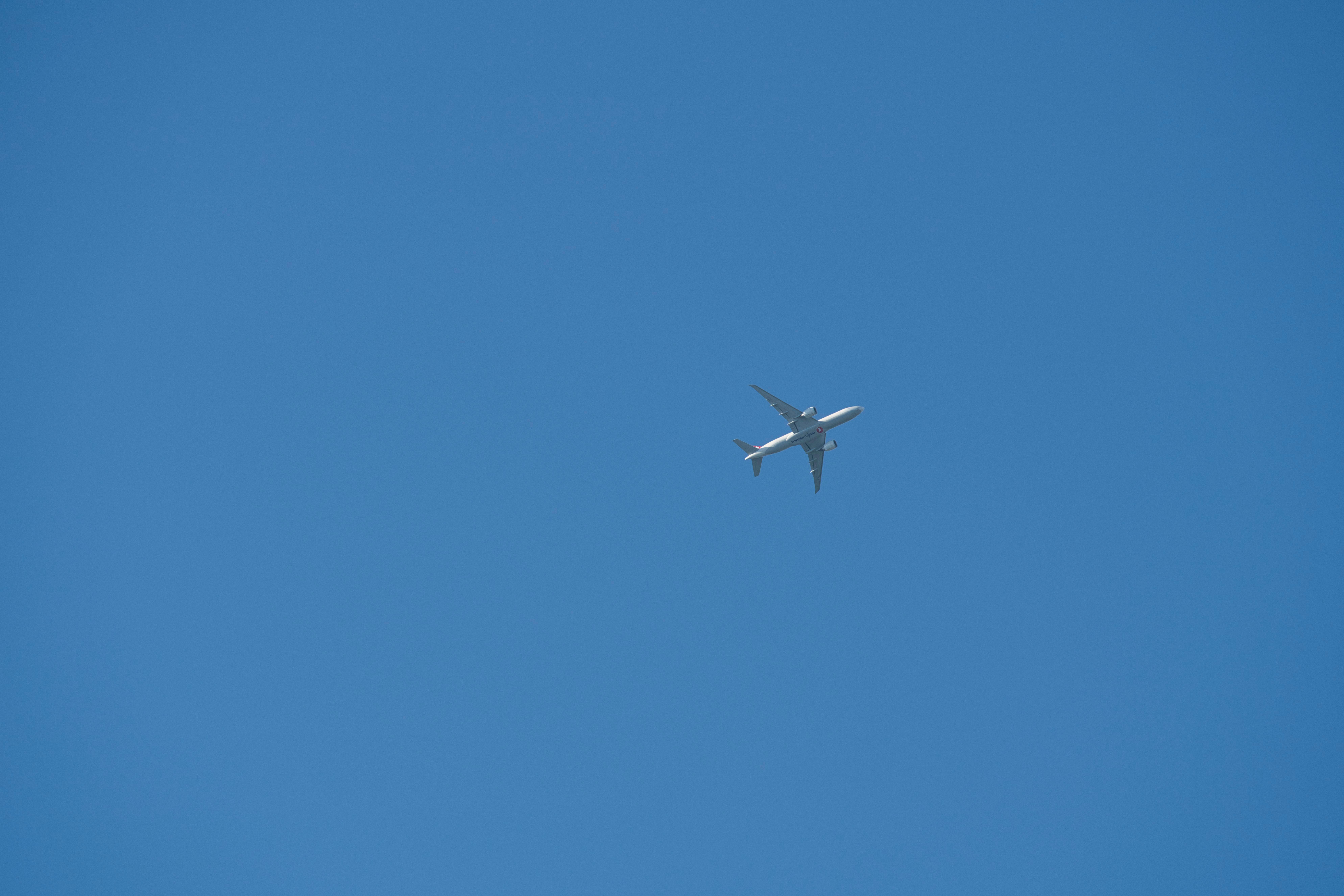 Free A commercial airplane soaring high against a clear blue sky, viewed from below. Stock Photo