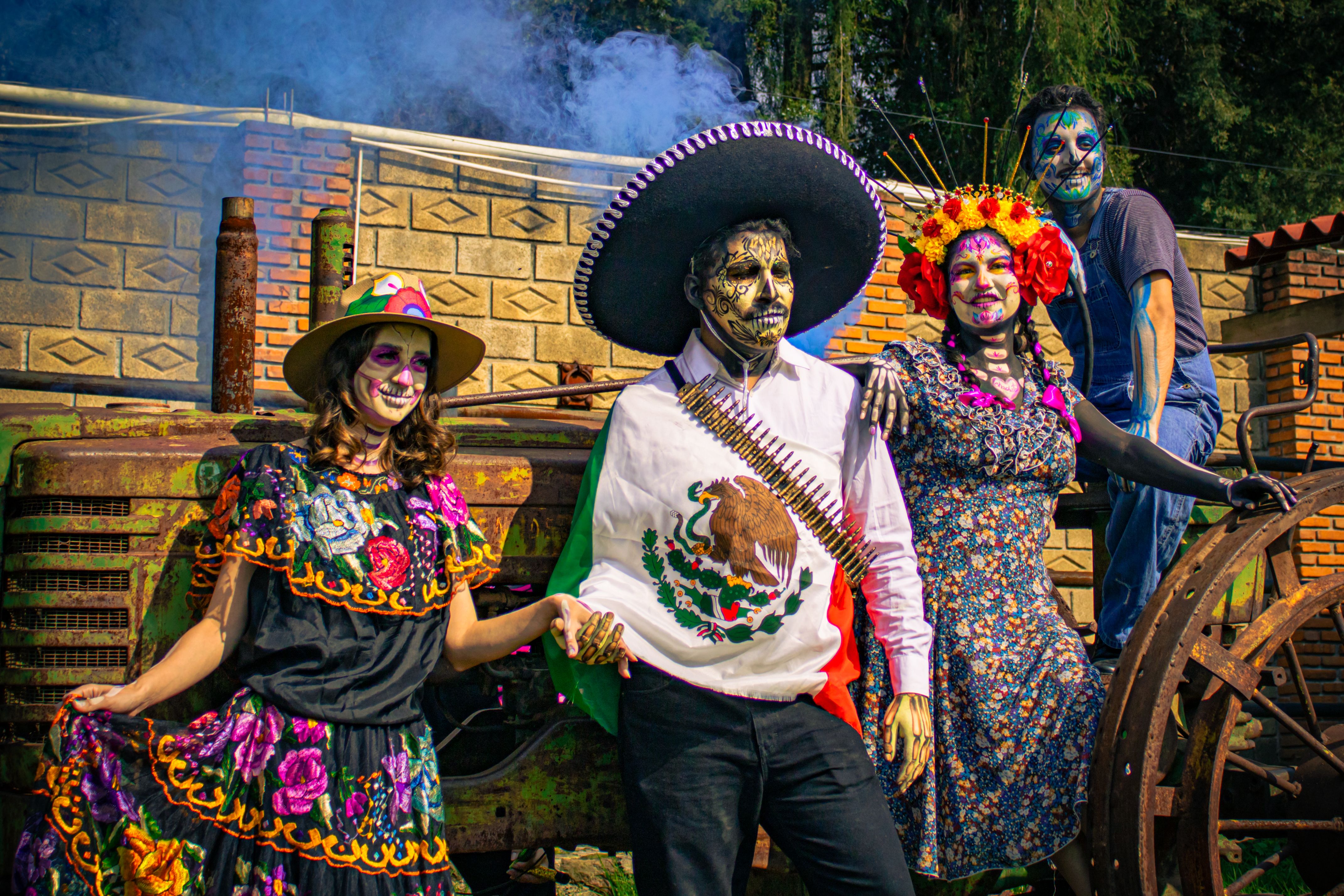Four people in Catrina costumes showcasing Mexican culture in a colorful outdoor setting.