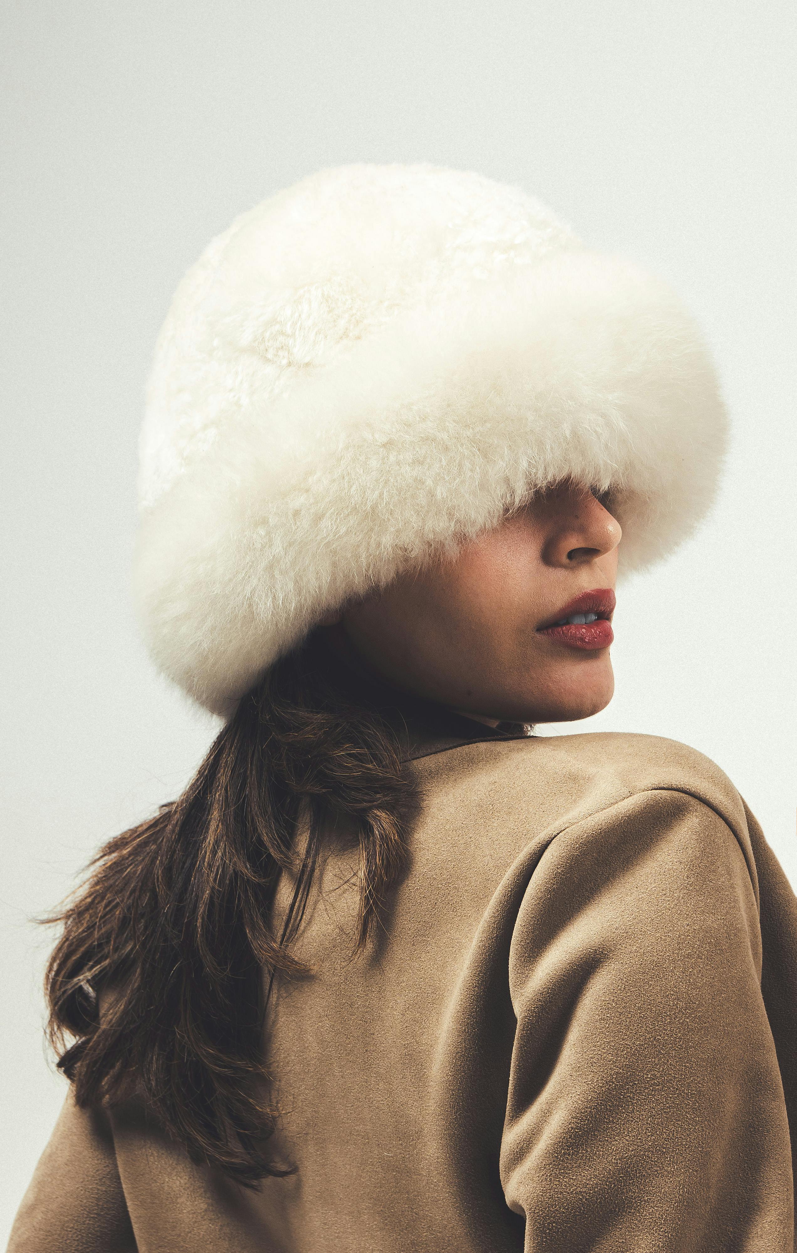 Elegant portrait of a woman wearing a white fur hat and brown coat.