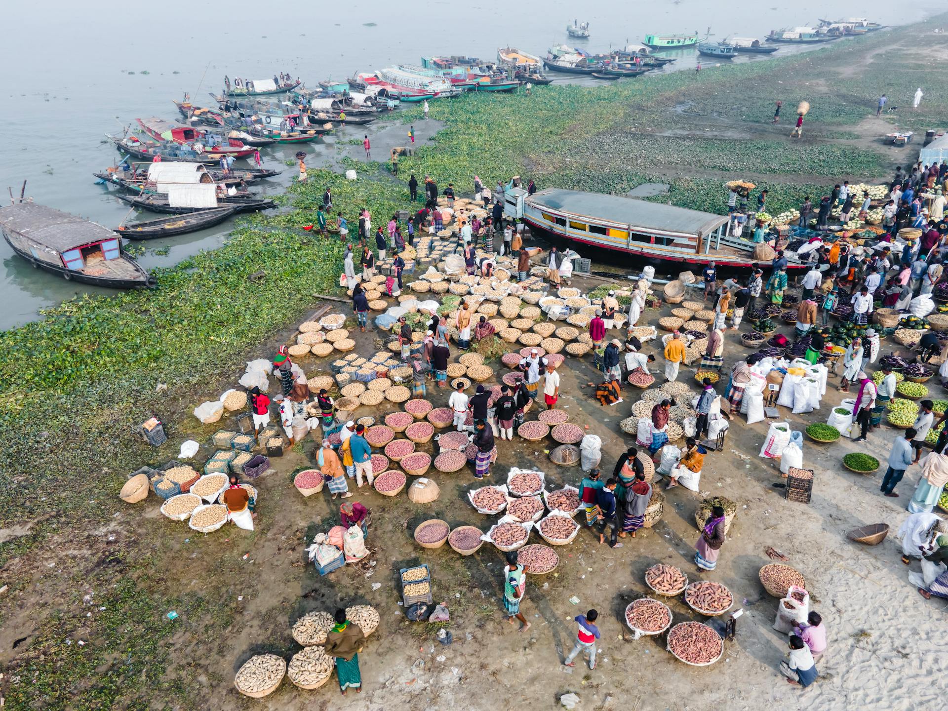 A vibrant aerial shot of a bustling riverbank market in Bangladesh with boats and vendors selling goods.