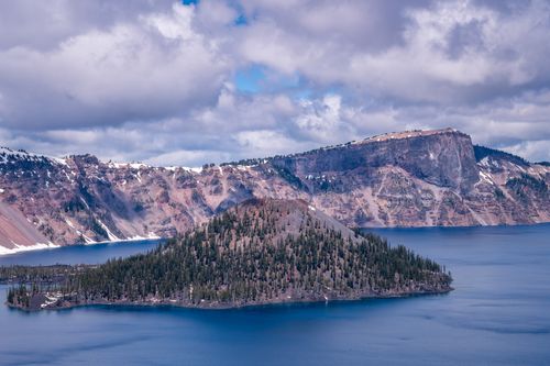Free Breathtaking view of Crater Lake with rocky cliffs and blue waters under cloudy skies. Stock Photo