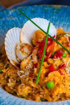 Mouthwatering seafood risotto with scallops, chili, and peas in a blue bowl.