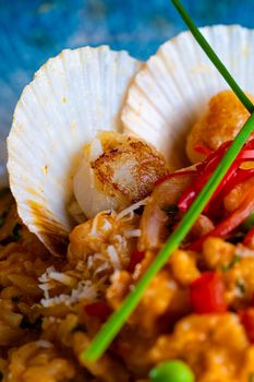 Close-up of a gourmet scallop risotto dish with vibrant peppers and cheese garnish.