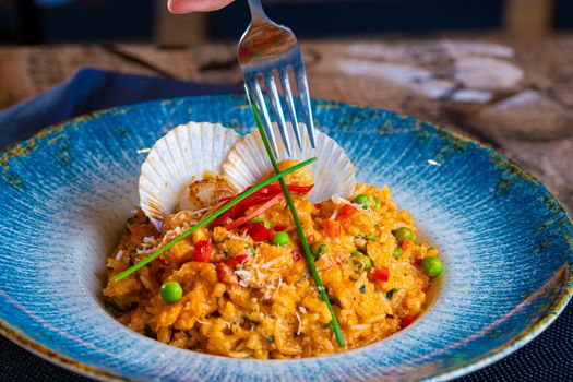 Vibrant seafood risotto with scallops and vegetables in a blue ceramic bowl.