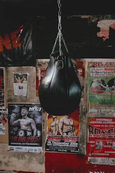 A vintage punching bag hangs amidst retro boxing posters in a gym.