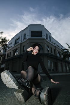 Woman in fashionable outfit posing confidently outside a modern building at dusk.