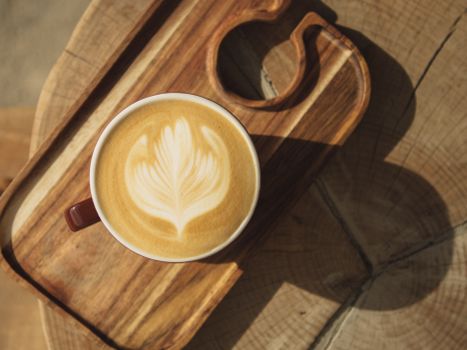 A latte with intricate leaf art served on a rustic wooden tray, perfect for cozy mornings.