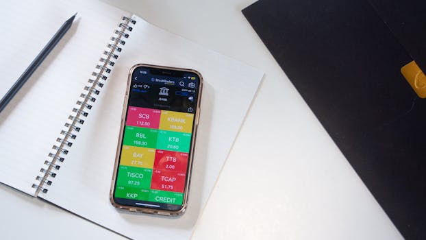 A smartphone displays a financial stock market app on a desk with a notebook and pencil.