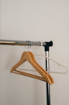 Simple wooden and plastic hangers on a metal rack in a minimalist setting.