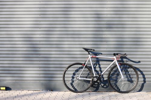 Free A sleek modern bicycle stands against a corrugated metal wall, casting shadows. Stock Photo