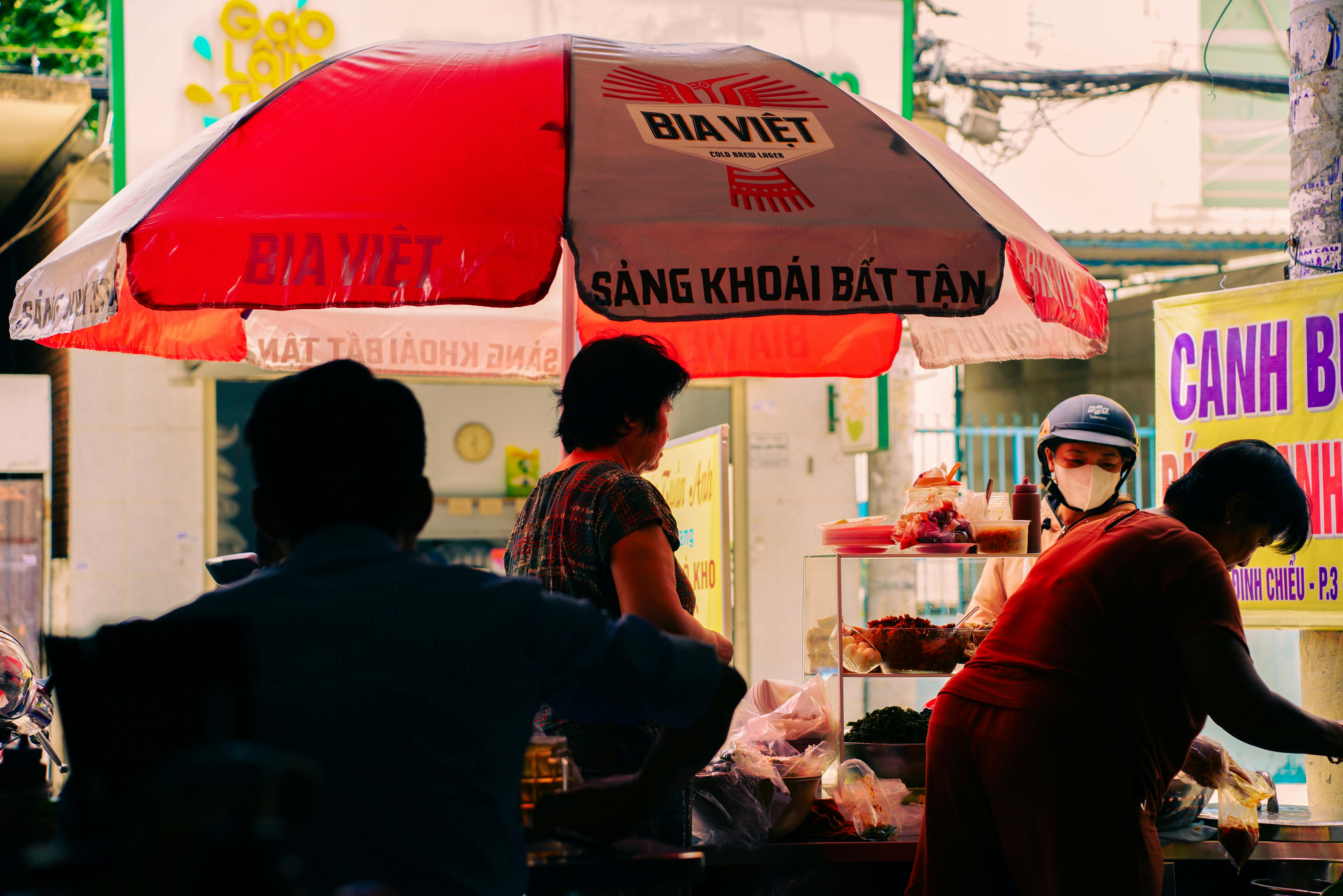 Street food vendors under red umbrella in vibrant Ho Chi Minh City, Vietnam's bustling market scene.