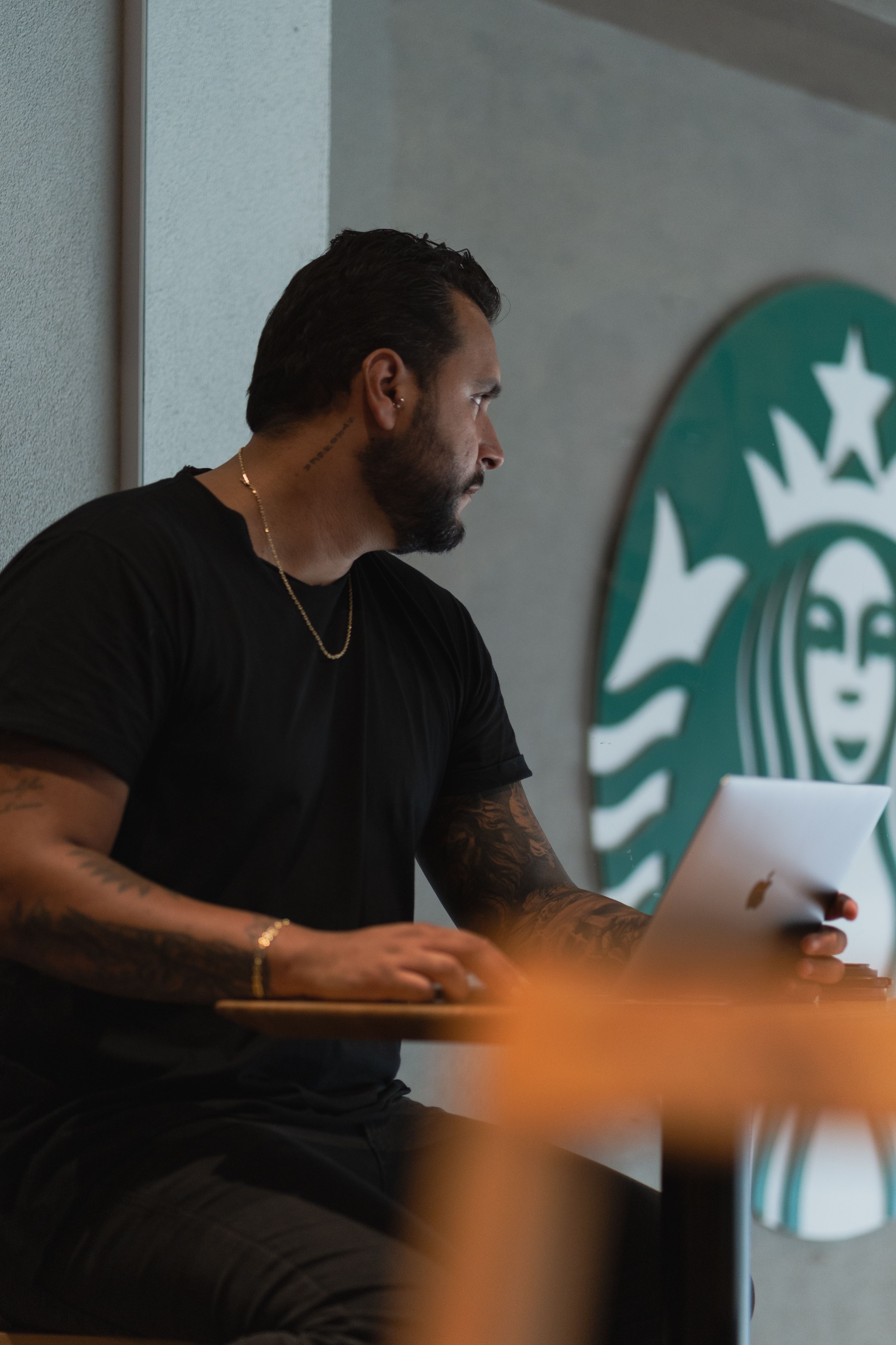 A man focused on his laptop in a coffee shop with a Starbucks logo.