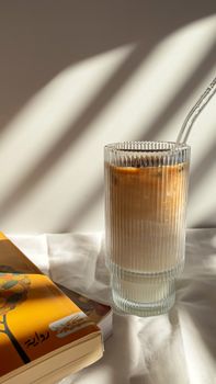 A refreshing iced latte beside a book, bathed in afternoon sunlight.