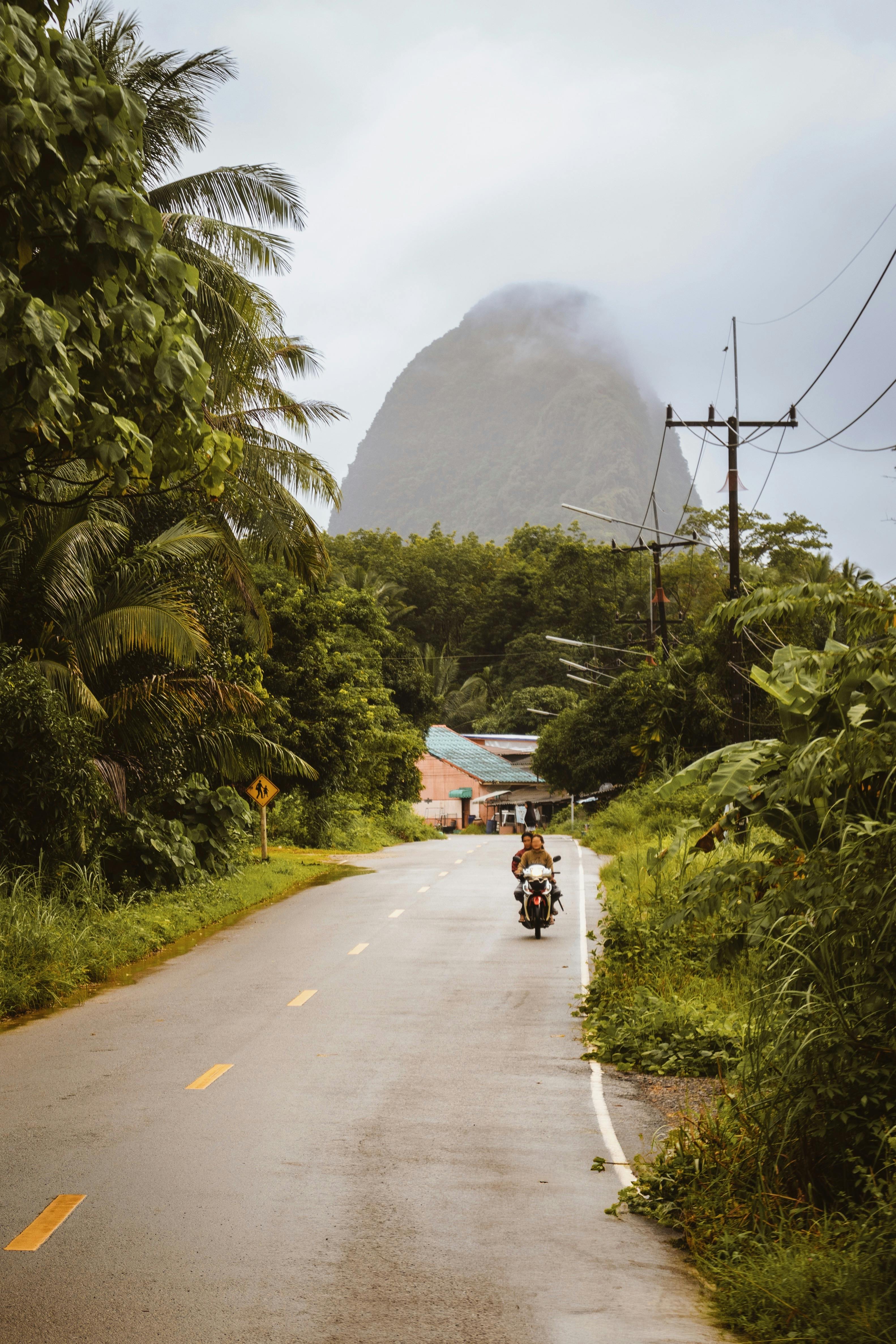 Motorbike riding on a scenic road with lush greenery and a mountain in Surat Thani, Thailand.