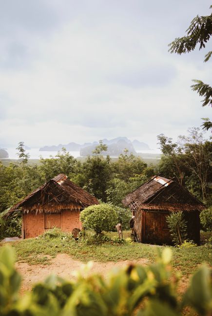 Serene view of traditional Thai huts amidst lush greenery with coastal backdrop in Koh Phangan, Thailand.