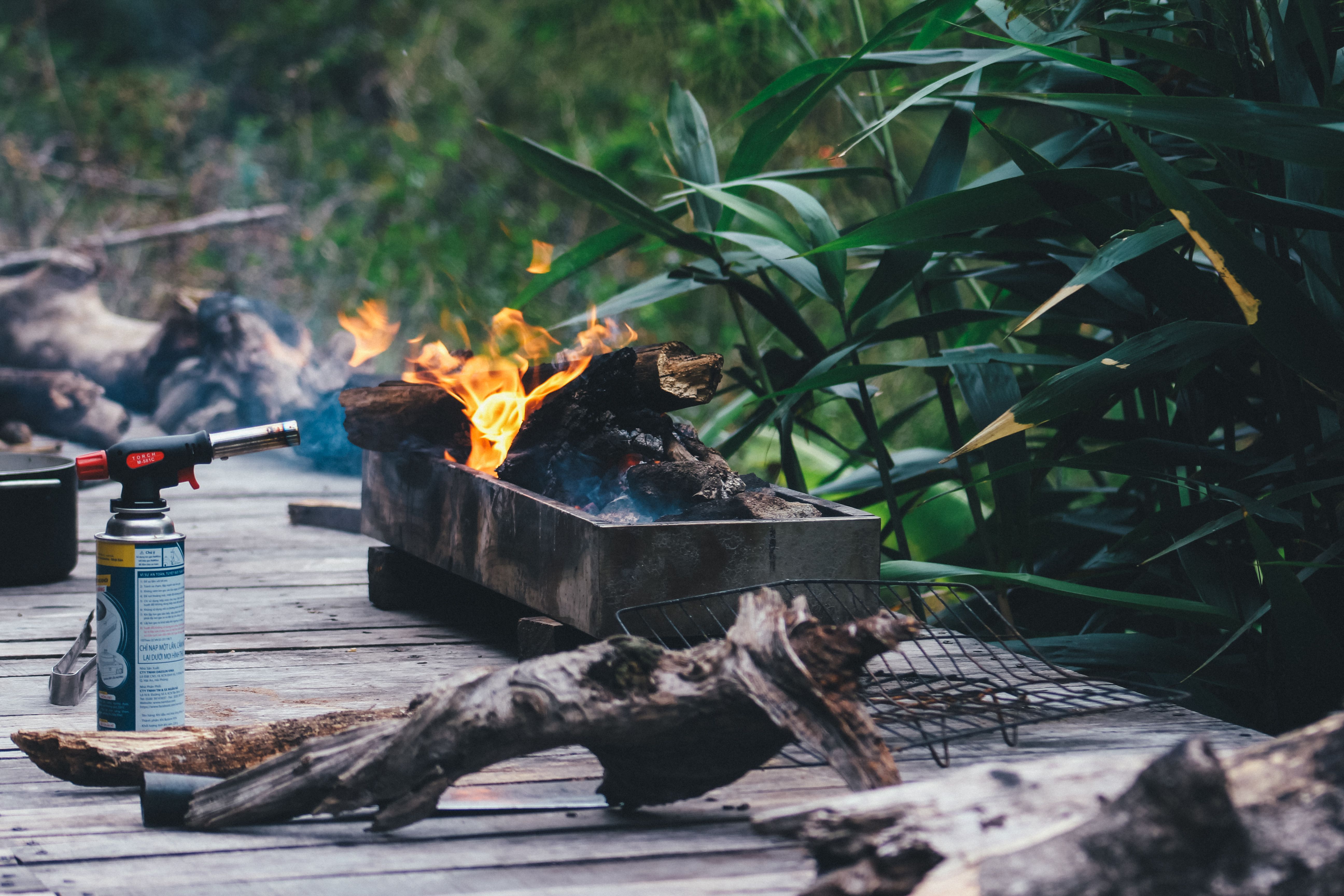 Rustic outdoor barbecue setup with logs and flamethrower in lush greenery.