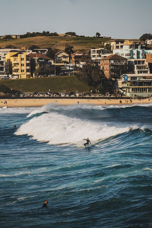 Free Surfer riding waves at a vibrant beach with urban backdrop, capturing the essence of coastal adventure. Stock Photo