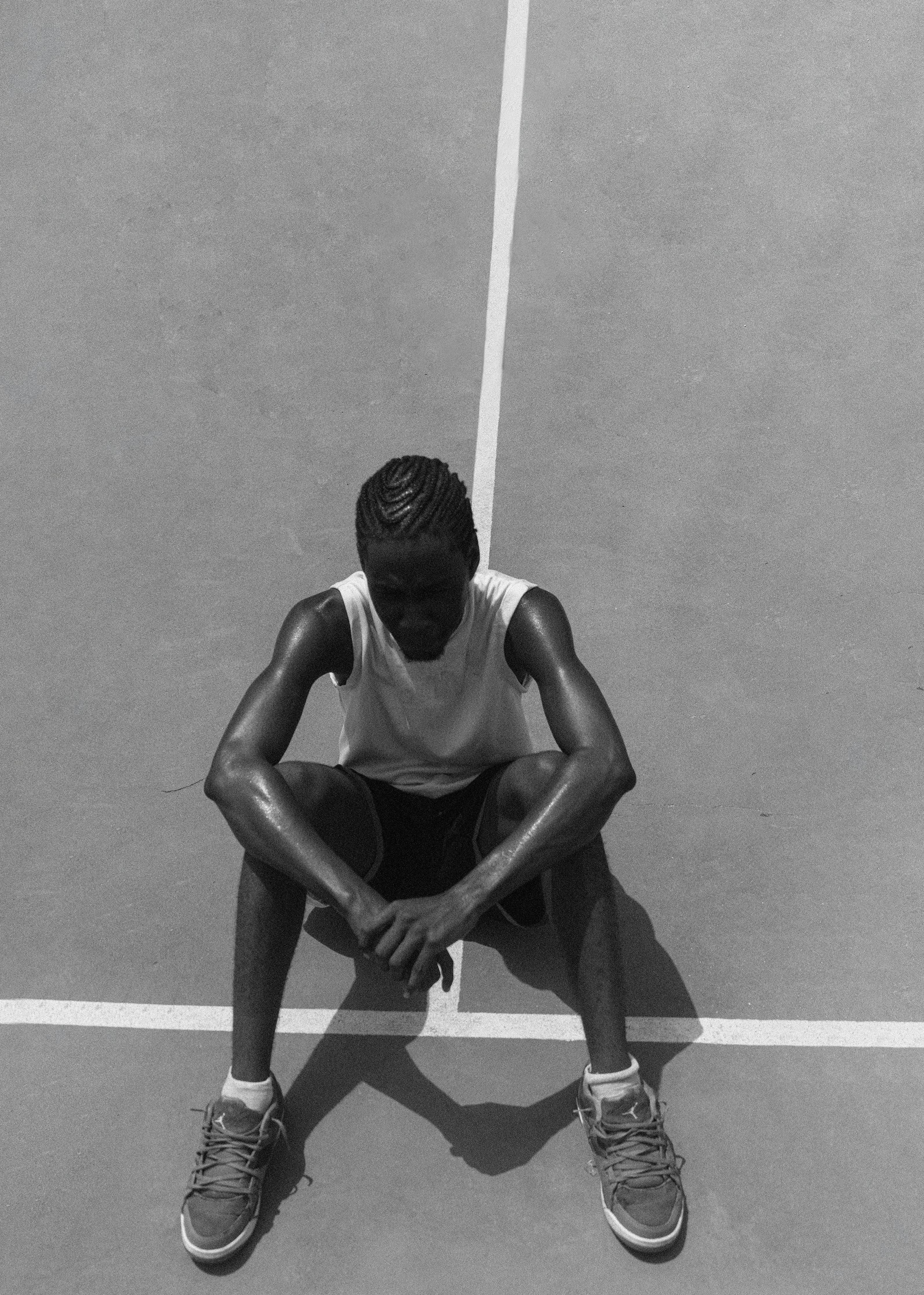 A contemplative black and white portrait of a young athlete resting on an outdoor court.