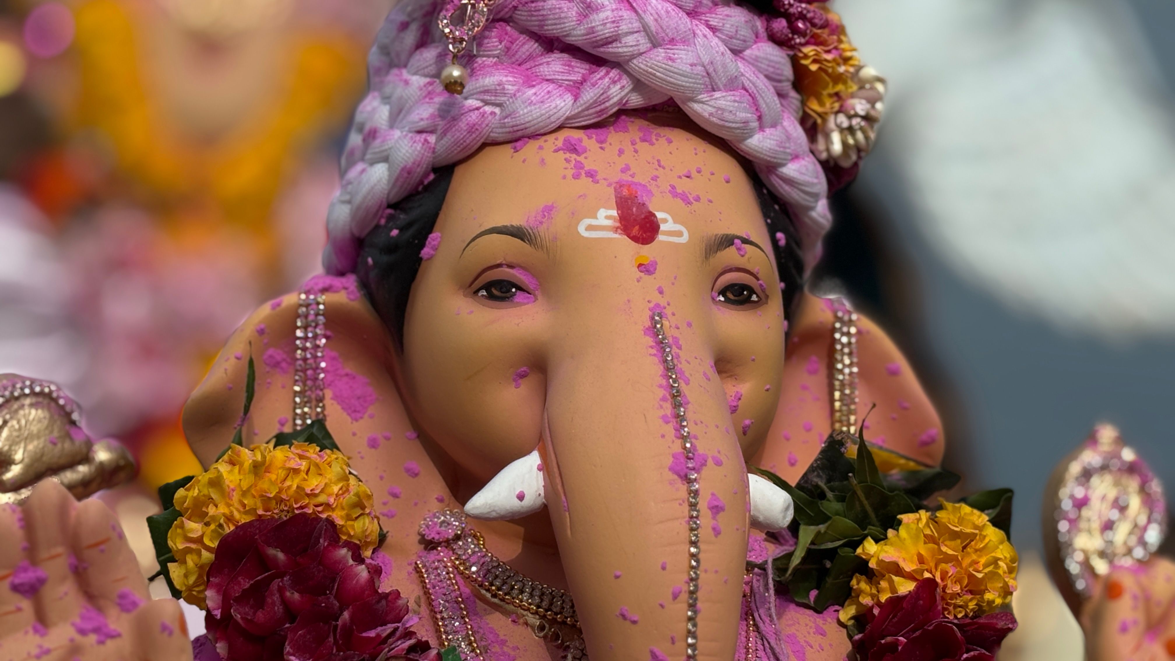 Close-up of a colorful Ganesh idol adorned with pink powders and floral decorations, symbolizing festive spirit.
