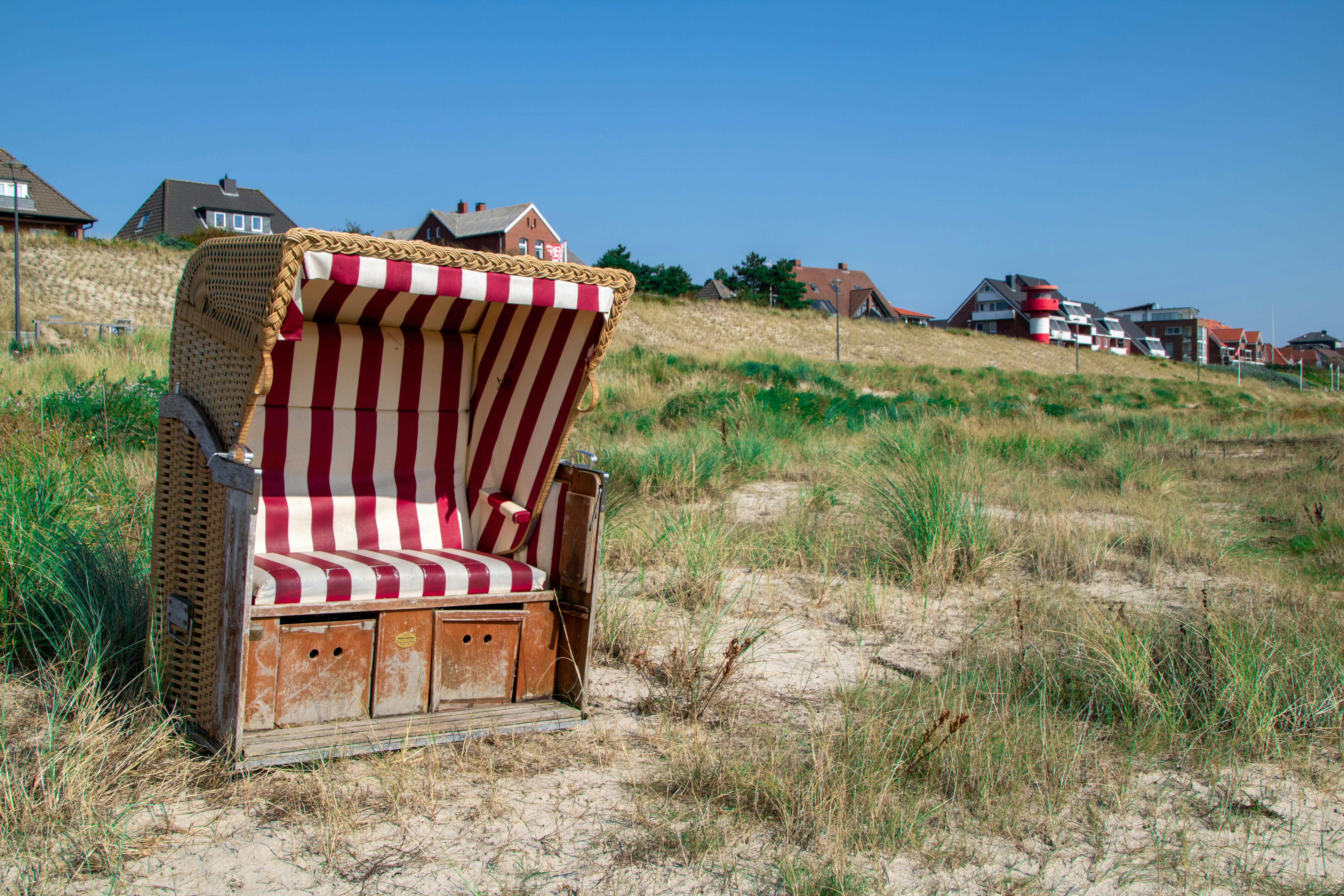 A beach basket with red stripes sitting on a sandy beach in Amrum, Germany, against a clear blue sky.