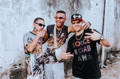 Free Three urban musicians posing energetically against a rustic wall, showcasing streetwear fashion. Stock Photo