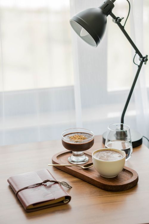 Free Relaxing coffee break setup with dessert, journal, and lamp on a wooden table. Stock Photo
